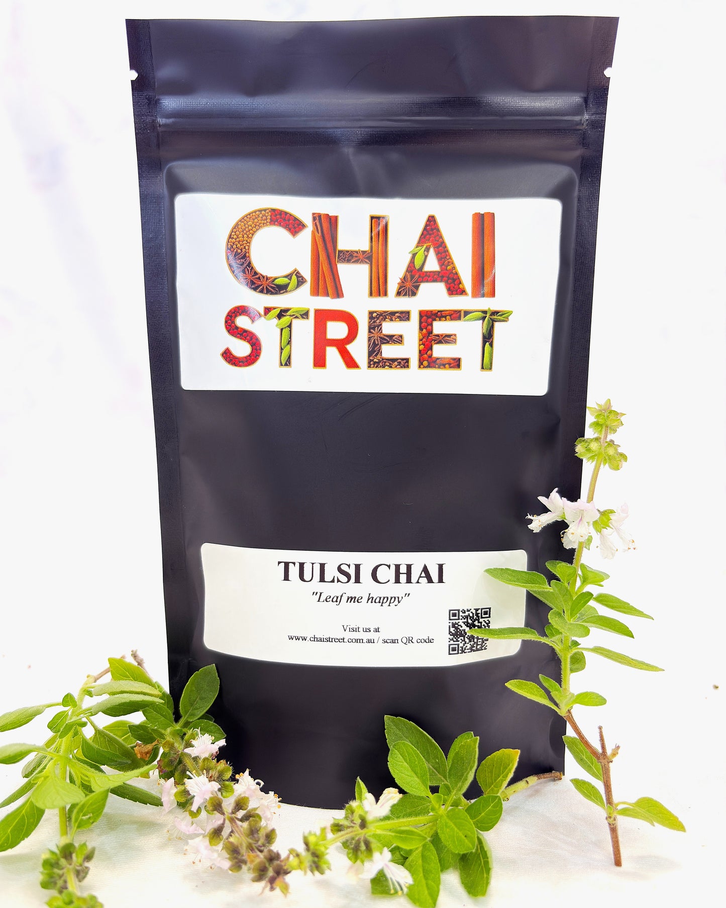 Tulsi Chai tea pouch with decorative holy basil leaves and white blossoms placed around it