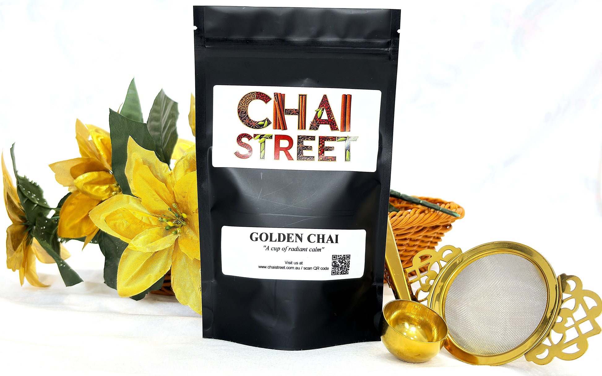 Chai Street Golden Chai tea pack displayed with golden flowers, tea scoop, and metal tea strainer
